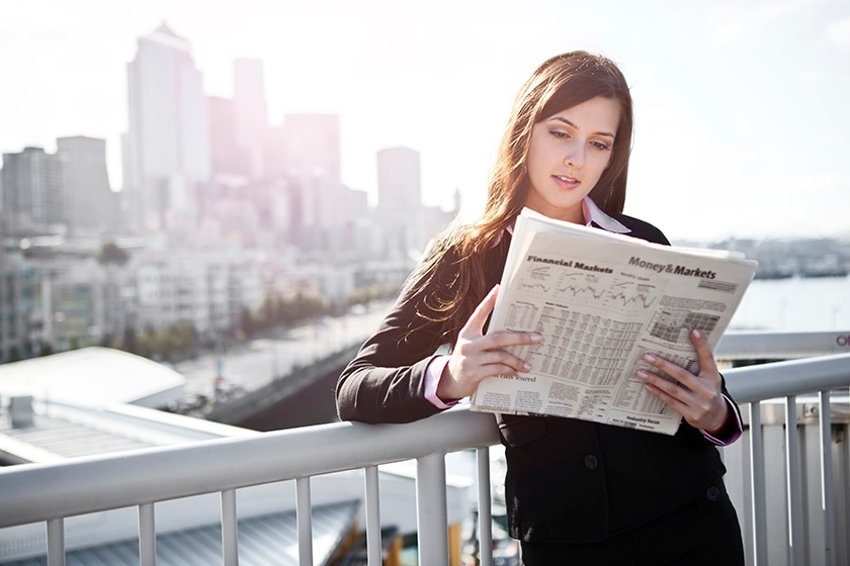 Frau, die an einem Zaun lehnt und Zeitung liest